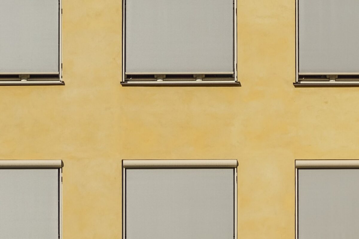 Modern building facade in Oslo with minimalist ochre walls and closed blinds creating a geometric pattern.